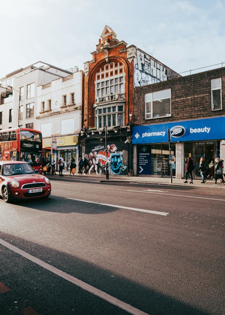 Street view of commercial buildings in Hampstead with a prominent historic brick façade featuring a large arched window and decorative architectural elements. The ground level has retail storefronts, 