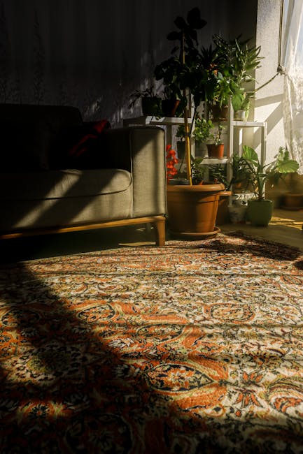 Close-up of a traditional patterned rug placed on a wooden floor near a black piece of furniture, such as a table or sofa, with the rug's edge featuring white fringe. The wooden flooring has a natural